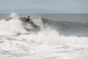 A surfer catching a left-hander, in the back the Nicoya Peninsula is visible.